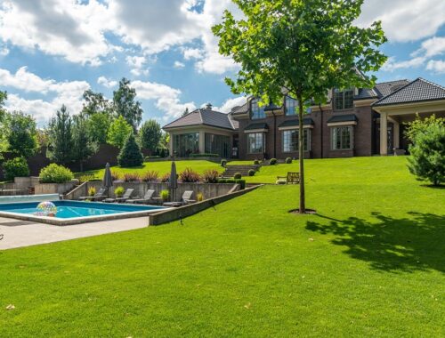 Healthy green backyard lawn after aeration with lush grass surrounding a modern home and swimming pool under a sunny sky